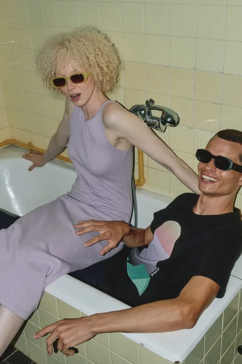 Frau und Mann mit Sonnebrillen und Bio-Kleidung von Dedicated sitzen lachend in einer Badewanne