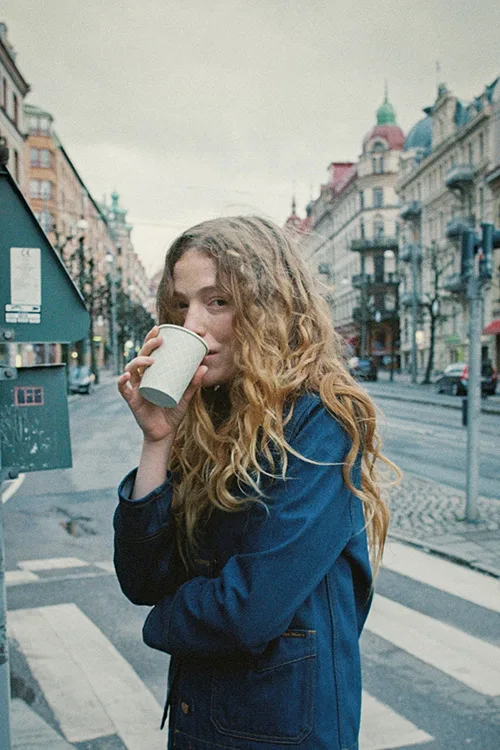 zündstoff-freiburg-nudie-jeans Kaffee trinkende Frau auf der Straße mit Jeansjacke von Nudie