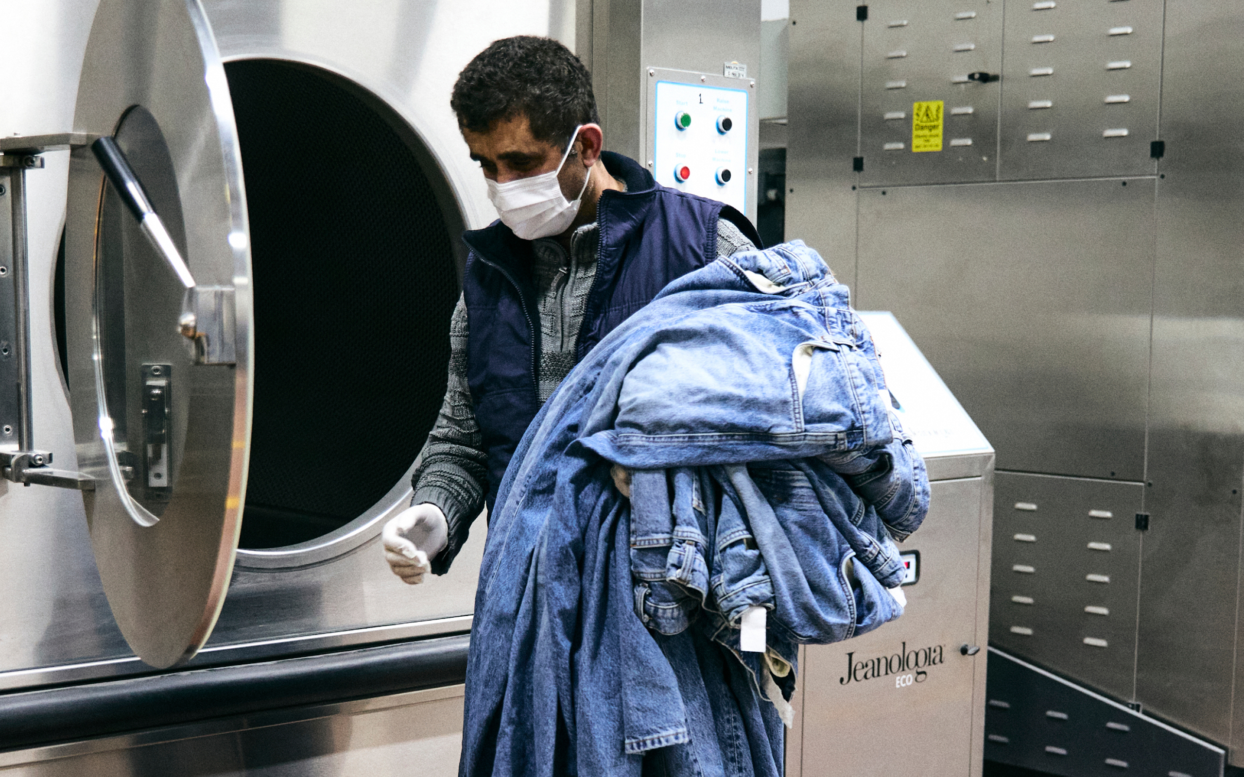 Jeans Produktion Ein Mann mit Jeans im Arm vor einer großen Waschmaschine